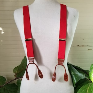 May include: Red suspenders with brown leather adjustable clips. The suspenders are made of a woven fabric and have a classic design.