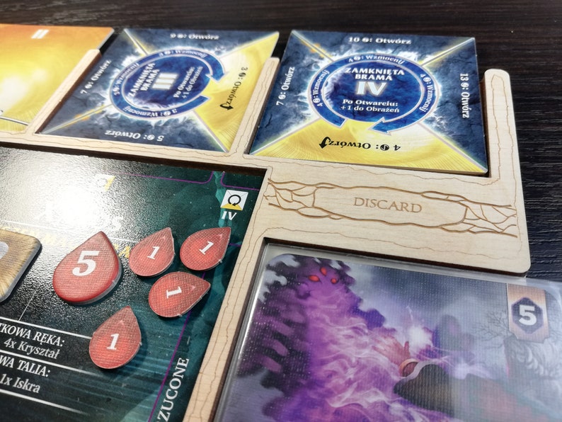 May include: A wooden game board with a discard pile, a deck of cards, and a set of tokens. The board is labeled "DISCARD". The cards are labeled "ZAMKNIĘTA BRAMA" and "IV". The tokens are numbered 1 and 5.