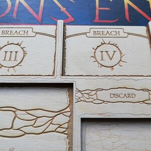 May include: Close-up of a wooden game board with two sections labeled "Breach" and a third section labeled "Discard". The Breach sections have Roman numerals III and IV, respectively.