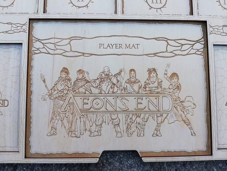 May include: A wooden player mat for the board game Aeon's End. The mat features a light brown background with a dark brown border and a stylized image of five characters from the game. The text "PLAYER MAT" and "AEON'S END" are printed on the mat.