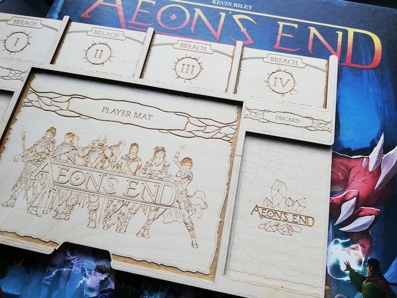 May include: A wooden game organizer for the board game Aeons End. The organizer has slots for the game's cards, a player mat, and a discard pile. The organizer is engraved with the game's logo and the text "Breach I, II, III, IV".