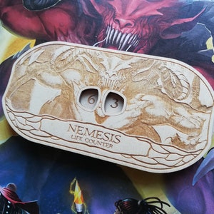May include: A wooden life counter for the board game Nemesis. The counter features a detailed image of a monster with a life counter that reads "603".