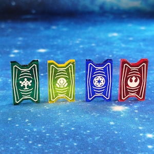 Op de afbeelding: Vier plastic tokens met verschillende gekleurde achtergronden en witte symbolen. De tokens zijn groen, geel, blauw en rood. De symbolen zijn een boom, een gloeilamp, een ster en een rebelliealliantie symbool.