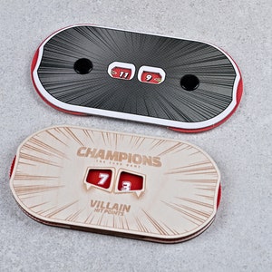 May include: Two game score trackers. The top one is black with red trim and displays scores of 11 and 9. The bottom tracker is tan with red trim and reads "Champions" and "Villain Hit Points", with scores of 7 and 3.
