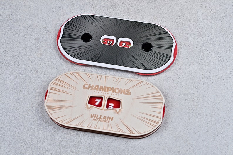 May include: Two game score trackers. The top one is black with red trim and displays scores of 11 and 9. The bottom tracker is tan with red trim and reads "Champions" and "Villain Hit Points", with scores of 7 and 3.