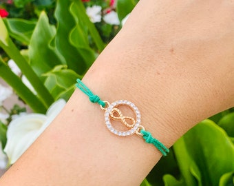 Pode incluir: Um bracelete de corda verde com um fecho de ouro em forma de símbolo de infinito incrustado com strass transparentes.