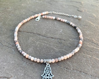 Pode incluir: Um delicado colar choker feito com pequenas contas multicoloridas e um pingente de mão de hamsa prateado.