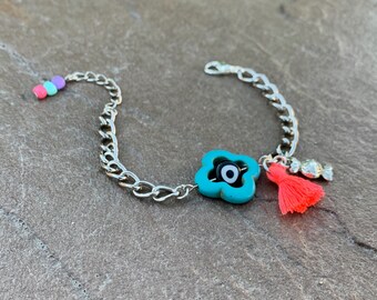 Pode incluir: Um bracelete de corrente prateada com um amuleto azul turquesa com um olho turco preto. O amuleto tem uma borla vermelha anexada.