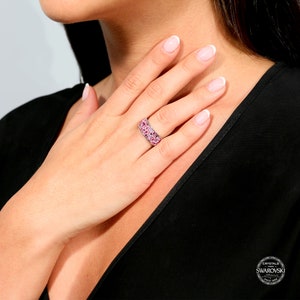 May include: A silver ring with a wide band set with pink crystals. The ring is made with crystals from Swarovski.