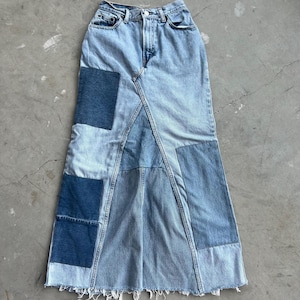 Peut inclure: Une longue jupe en jean faite de différentes nuances de denim bleu, avec un design patchwork. La jupe a une taille haute et une silhouette évasée.