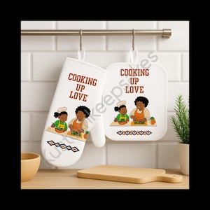 Peut inclure: Un ensemble de manique et de dessous de plat blancs avec le texte "COOKING UP LOVE" et une illustration de deux personnes en train de cuisiner. Le dessous de plat et la manique sont suspendus à une barre métallique. Une planche à découper en bois et une petite plante sont également visibles.