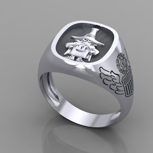 May include: A silver ring with a black and white design. The ring features a cartoon character wearing a hat and holding a staff. The ring also has a wing and shield design on the side.