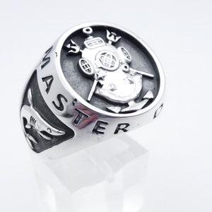 May include: A silver ring with a detailed design of a diving helmet, two tridents, and an anchor. The ring is inscribed with the words "MASTER DIVING".