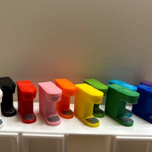 以下が含まれることがあります： 白、黒、赤、ピンク、オレンジ、黄色、緑、青、紫など、さまざまな色のカラフルなミニチュアコーヒーメーカーのコレクション。それぞれ長方形のベースと丸みを帯びた上部があります。