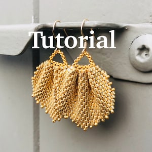 May include: Gold beaded earrings with a fan-shaped design. The earrings are hanging from a metal hook.