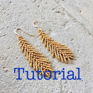 May include: Gold beaded earrings with a feather-like design. The earrings are hanging from a white surface. The word "Tutorial" is written in blue letters below the earrings.