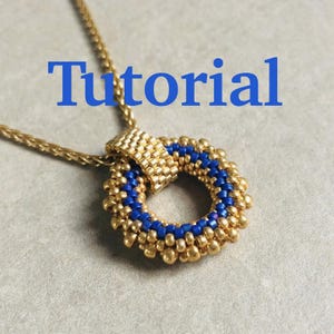 May include: Gold-toned necklace with a circular pendant. The pendant features a ring of blue beads surrounded by gold beads. The word "Tutorial" is written in blue across the top of the image. The necklace chain is also gold.