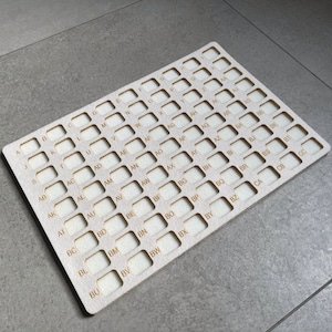 Op de afbeelding: Een houten bord met een raster van vierkanten, elk gelabeld met een lettercombinatie, beginnend met "A" en eindigend met "CO".