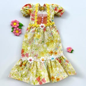 May include: A yellow and white floral print dress with a lace trim and orange and yellow accents. The dress has a ruffled hem and is decorated with small flowers.