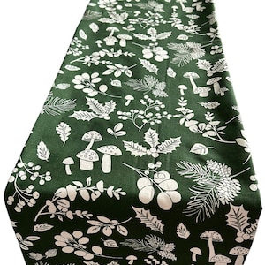 May include: A green table runner with a white mushroom, holly, and pine needle pattern.