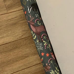 May include: A green doorstop with a woodland animal print. The print features deer, squirrels, and other forest creatures on a dark green background with orange and pink flowers.