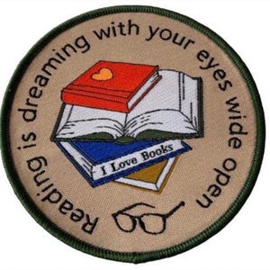 May include: A round, tan-coloured patch with green stitching around the edges. The patch features a stack of books with the text "I Love Books" on the top book. The text "Reading is dreaming with your eyes wide open" is written around the edge of the patch.