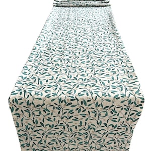 May include: A long, rectangular table runner featuring a repeating pattern of teal leaves and small white berries on a cream background. The runner is folded at the top, displaying the fabric's design. Suitable for adding a decorative touch to a dining table.