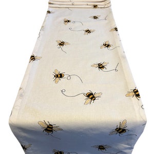 May include: White table runner with a repeating pattern of yellow and black bees. The bees are flying and have a small black line trailing behind them.