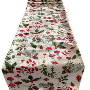 May include: Cream-coloured table runner with a repeating pattern of red mushrooms, holly, berries, and pinecones. The design features green leaves and brown pinecones, creating a festive, nature-inspired aesthetic. The runner is made of a soft fabric.