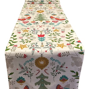 Könnte beinhalten: Weißer Weihnachtstischläufer mit festlichem Muster. Das Design umfasst grüne Weihnachtsbäume, rote und gelbe Sterne und stilisierte Vögel. Der Läufer ist mit roten, grünen und goldenen Ornamenten und Schneeflocken verziert.