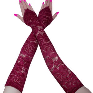May include: A pair of long, fingerless gloves crafted from deep burgundy lace. The fabric features an intricate floral pattern with openwork detailing. These opera-length gloves extend from the knuckles up to the mid-forearm, providing full coverage.