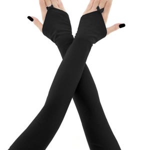 May include: Black fingerless gloves with long sleeves. The gloves have a small bow detail at the wrist and are made of a soft, stretchy material. The image shows the gloves worn with black nail polish.