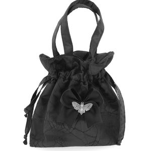 Pode incluir: Bolsa preta com cordão, com um padrão texturizado e duas alças. Um grande laço preto está centrado na frente, adornado com um adorno prateado em forma de traça. A bolsa tem um top franzido e um acabamento acetinado.