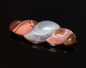 May include: A silver brooch featuring a cluster of three agate stones. The stones are a mix of pink, white, and brown with swirling patterns.