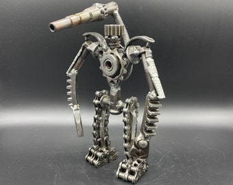 May include: A robot made of metal gears and chains. The robot is standing on a black surface and has a long, thin arm that is pointing forward.