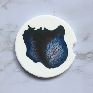 May include: A white round coaster with a blue and black floral design. The design is a close-up of a flower petal.