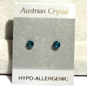 May include: Two teal-colored, round crystal stud earrings on a gray card. The card has the text "Austrian Crystal" in gold lettering at the top and "HYPO-ALLERGENIC" at the bottom.