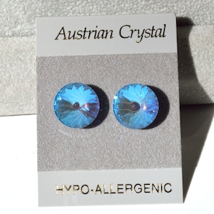 May include: A pair of round, iridescent blue Austrian crystal stud earrings. The earrings are displayed on a gray card with the text "Austrian Crystal" and "HYPO-ALLERGENIC" in gold lettering.