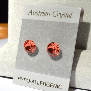 May include: A pair of red crystal stud earrings on a white card with the text "Austrian Crystal" and "Hypo-allergenic".