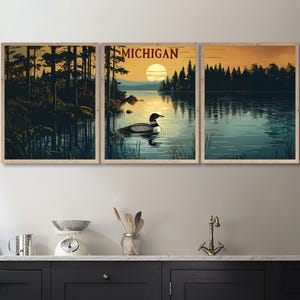 May include: Triptych wall art featuring a serene lake scene with a loon, trees, and a sunset. The word "MICHIGAN" is displayed above the central panel. The artwork is framed in light-colored wood, creating a rustic aesthetic.