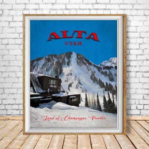 May include: Framed poster featuring a winter landscape with snow-covered mountains and a lodge. The word "ALTA" is in red, above "UTAH". The phrase "Land of Champagne Powder" is at the bottom, in red script. The poster is in a wooden frame.
