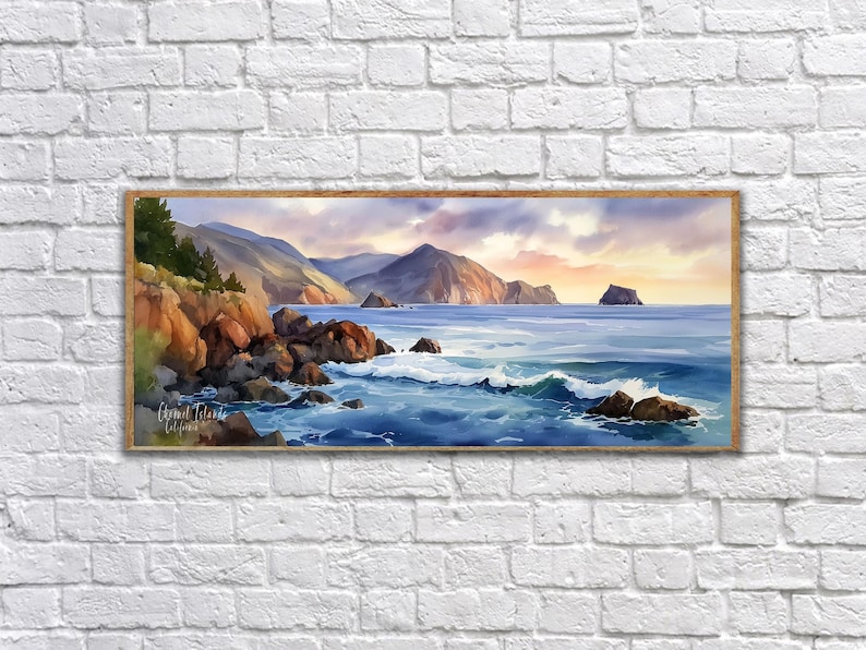 K&ouml;nnte beinhalten: Gerahmtes Aquarellgem&auml;lde einer K&uuml;stenlandschaft. Das Kunstwerk zeigt eine felsige K&uuml;stenlinie mit brechenden Wellen, Bergen im Hintergrund und einen farbenfrohen Sonnenuntergang. Das Gem&auml;lde befindet sich in einem Holzrahmen und ist an einer wei&szlig;en Backsteinmauer befestigt.