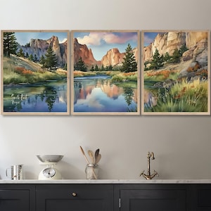 May include: A triptych of framed watercolor landscape paintings. The artwork depicts a river scene with mountains, trees, and reflections in the water. The color palette includes blues, greens, and earth tones, with a light wood frame.