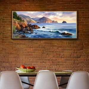 K&ouml;nnte beinhalten: Gerahmtes Landschaftsgem&auml;lde, das eine K&uuml;stenlandschaft mit felsigen Ufern, tosenden Wellen und Bergen unter einem Sonnenuntergangshimmel zeigt. Das Kunstwerk zeigt Farbt&ouml;ne von Blau, Braun und Orange und schafft eine ruhige und naturalistische Ansicht.