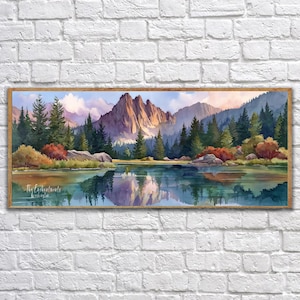 May include: Watercolor landscape art print featuring a mountain range, lake, and evergreen trees. The artwork has a wooden frame and is mounted on a white brick wall. The image reflects the mountains and trees in the lake. The text "The Enchanted Woods" is visible.
