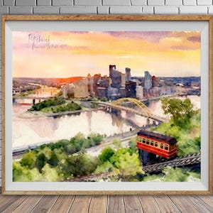 Peut inclure: Peinture à l'aquarelle de Pittsburgh, Pennsylvanie, représentant l'horizon de la ville, des ponts et un funiculaire rouge et jaune. L'œuvre est encadrée dans un cadre en bois et posée contre un mur de briques.