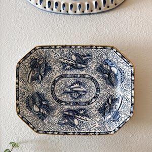 May include: A rectangular ceramic platter with clipped corners featuring a blue and white transferware pattern of seashells and coral. The design includes a central oval medallion surrounded by four shell clusters and a gold-toned rim.