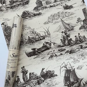 May include: A roll of Seabrook Design wallpaper featuring a black and white nautical toile pattern. The design includes illustrations of boats, people, and buildings. The roll is partially unrolled, revealing the pattern and the brand label.