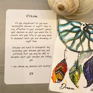 K&ouml;nnte beinhalten: Eine wei&szlig;e Karte mit dem Wort "Dream" in schwarzer Schrift. Die Karte enth&auml;lt ein Zitat &uuml;ber Tr&auml;ume und Tagebuchf&uuml;hrung. Die Karte liegt neben einem bunten Traumf&auml;nger mit Federn.