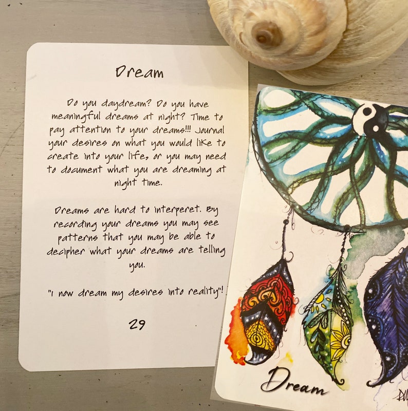 K&ouml;nnte beinhalten: Eine wei&szlig;e Karte mit dem Wort "Dream" in schwarzer Schrift. Die Karte enth&auml;lt ein Zitat &uuml;ber Tr&auml;ume und Tagebuchf&uuml;hrung. Die Karte liegt neben einem bunten Traumf&auml;nger mit Federn.